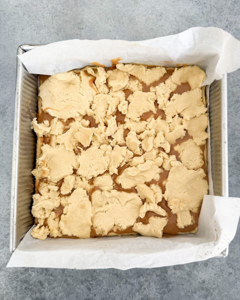 Caramel topped with cookie dough in a square baking pan.