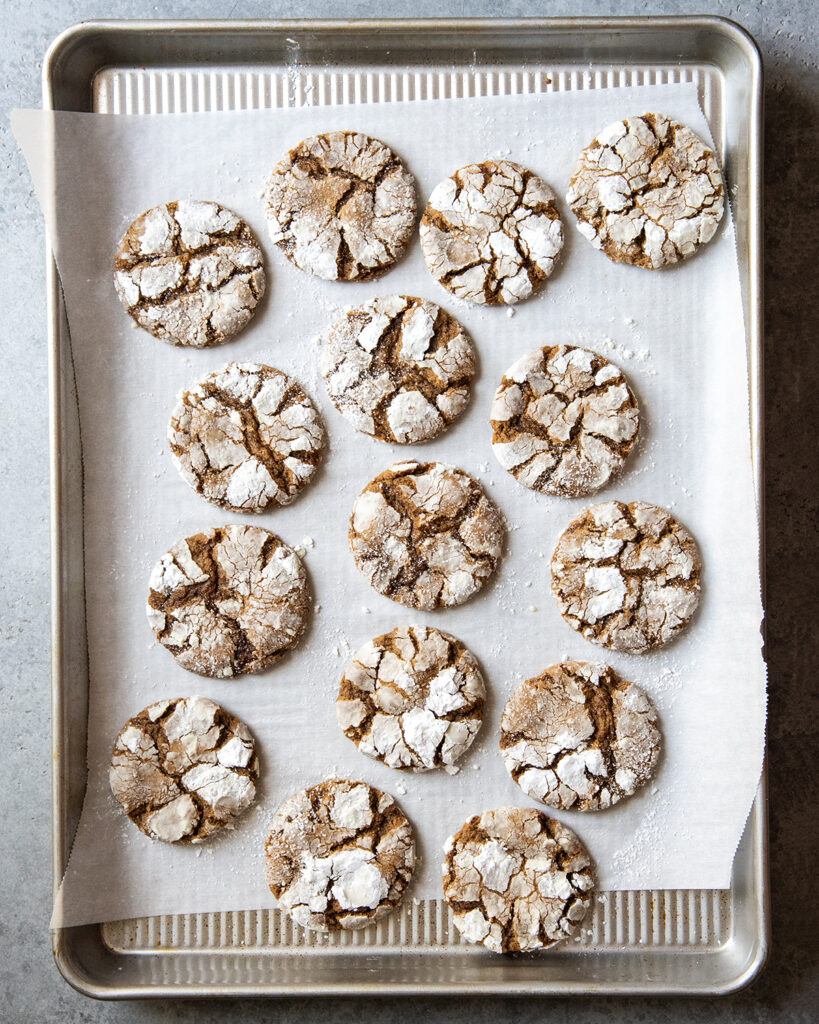 A cookie sheet topped with molasses crinkle cookies, coated in powdered sugar.