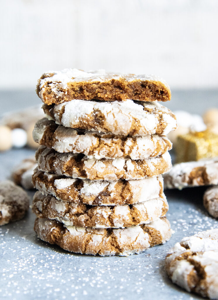 A stack of several ginger molasses crinkle cookies coated in powdered sugar, the top cookie is broken in half showing the center of it.