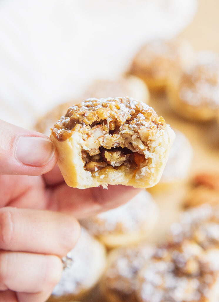 A hand holding a bite sized pecan tassies, with a bite taken out of the front showing the inside of it.