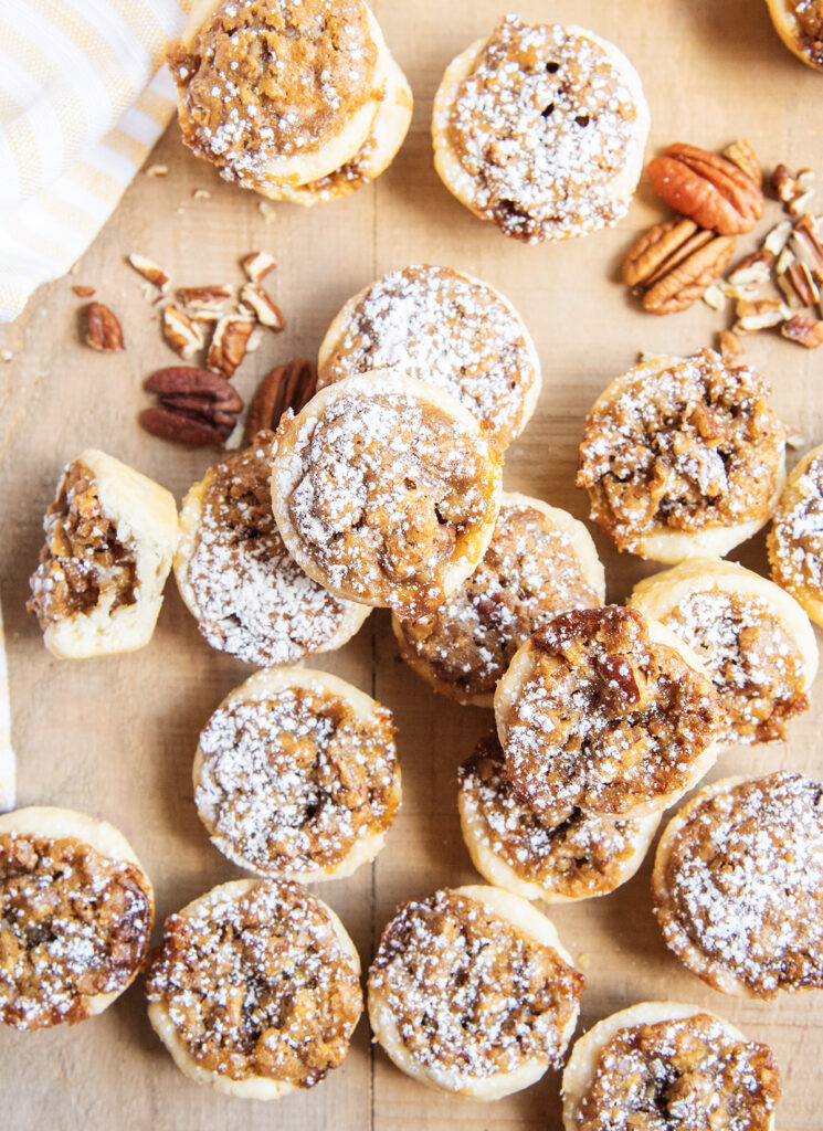 An above view of pecan tassie on a wooden table, they are topped with powdered sugar.