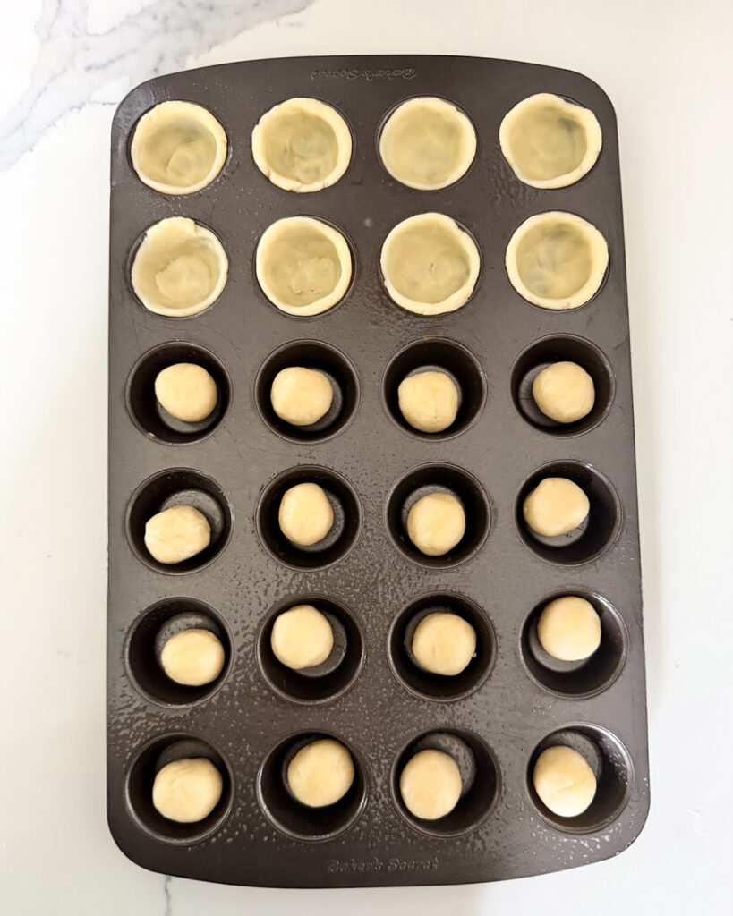 Balls of dough, and some are pressed into a mini muffin pan.