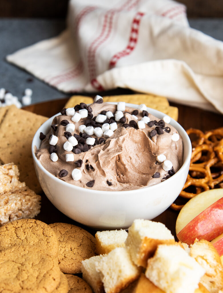 A bowl of hot chocolate dip with some scooped out, and it is topped with mini chocolate chips and marshmallows.