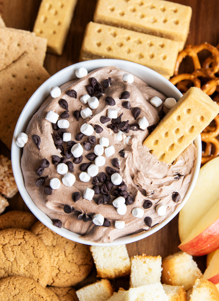 A close up of a bowl of chocolate fruit dip topped with mini chocolate chips, with a shortbread cookie sticking in the bowl. 