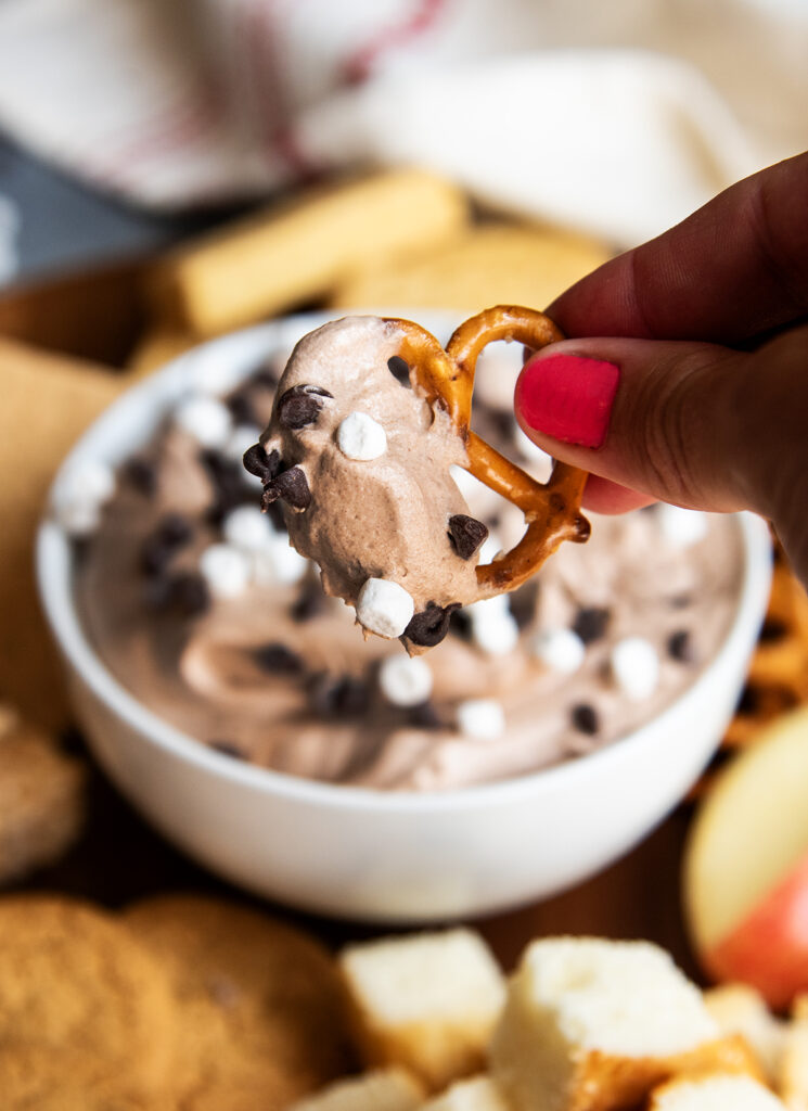 A hand holding a pretzel topped with hot chocolate dip.
