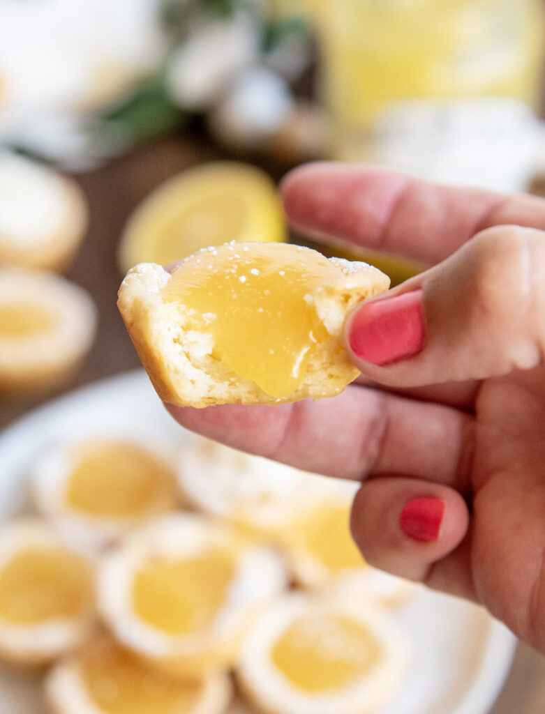 A hand holding a lemon tassie cup with a bite out of it.