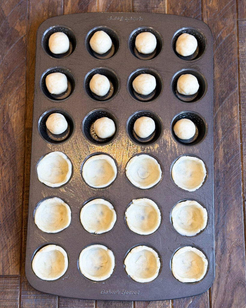 Balls of dough, and some are pressed into a mini muffin pan.