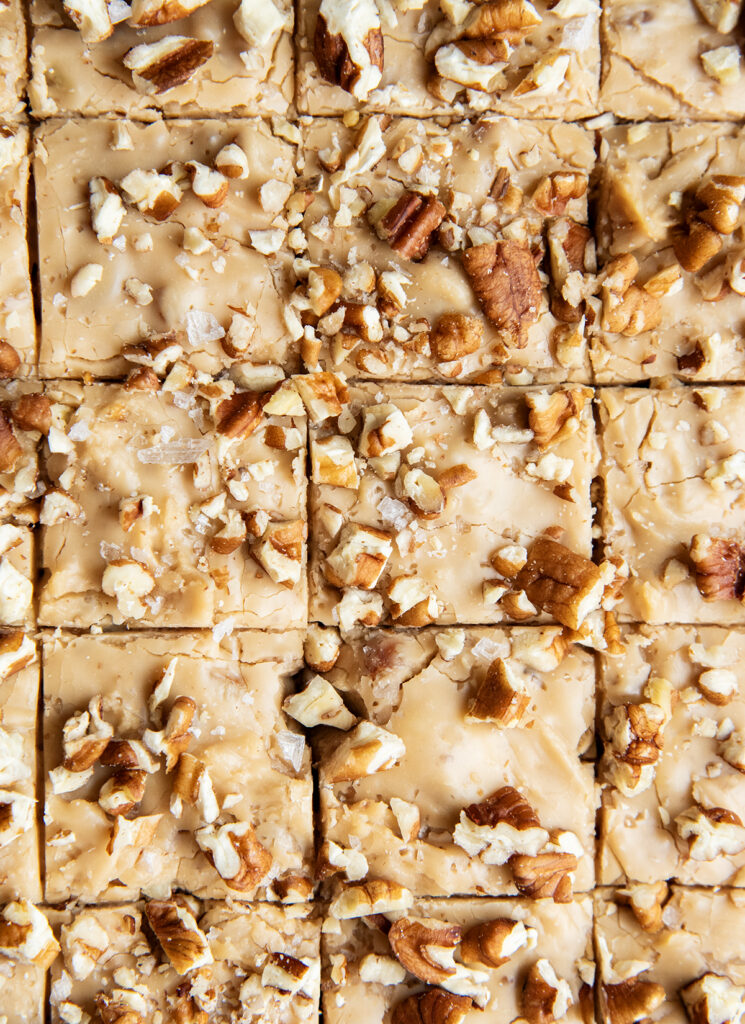 An above view of rows of penuche fudge topped with pecans on a piece of parchment paper.