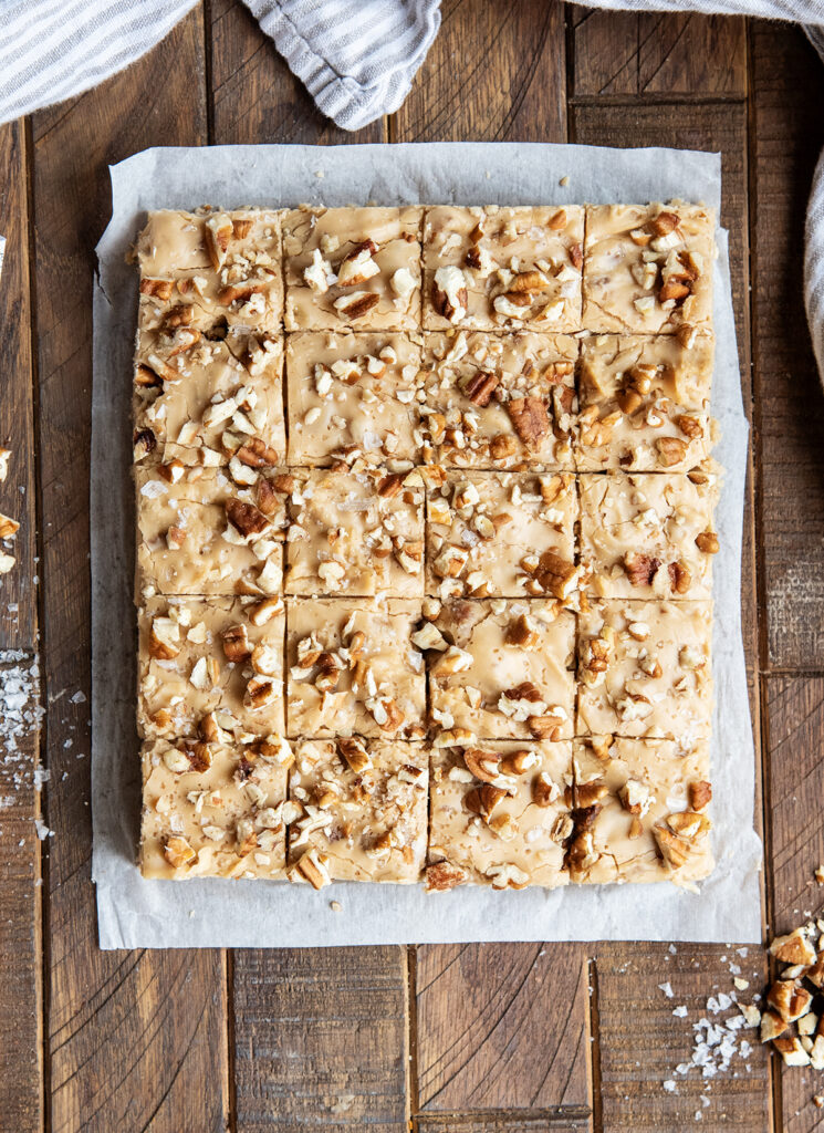 An above view of rows of penuche fudge topped with pecans on a piece of parchment paper.