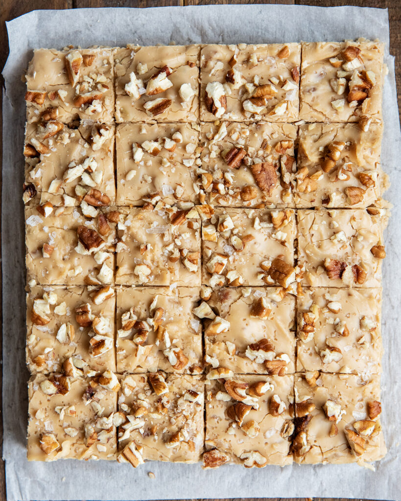An above view of rows of penuche fudge topped with pecans on a piece of parchment paper.