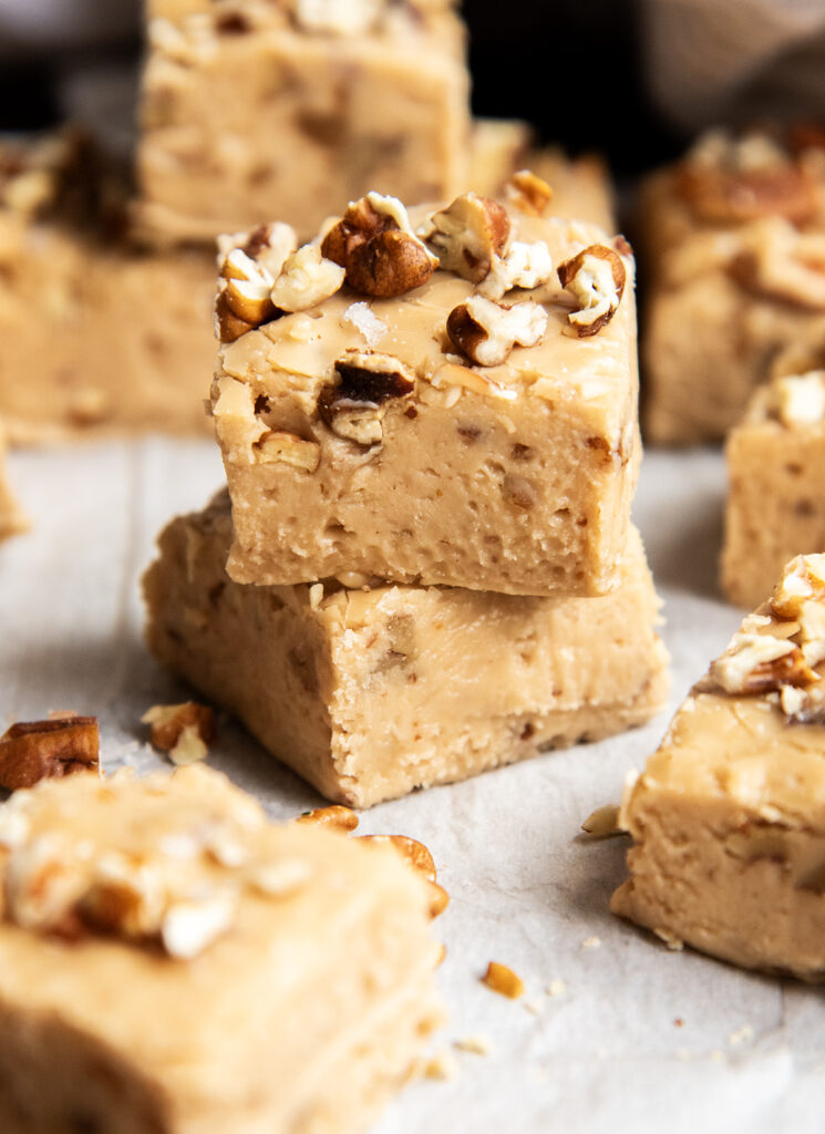 A stack of two pieces of pecan brown sugar penuche fudge topped with chopped pecans.