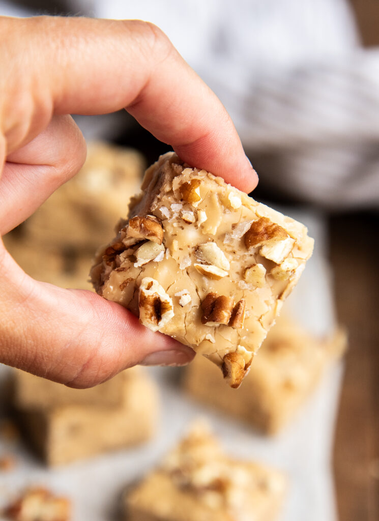 A hand holding a piece of pecan penuche fudge.