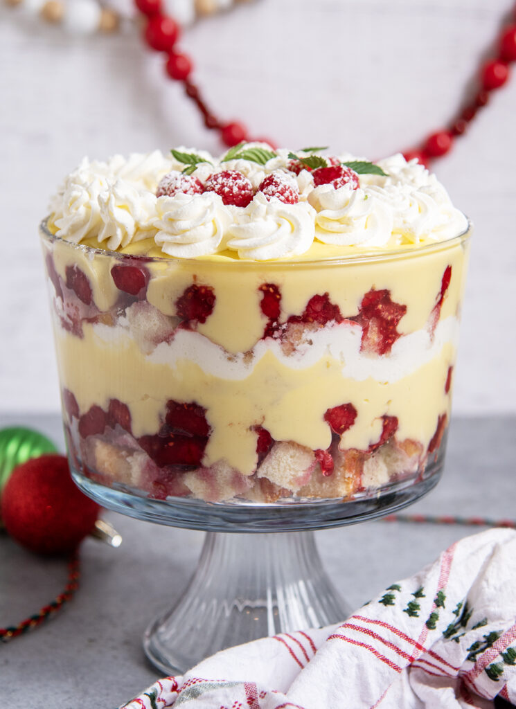 A side view of a trifle in a trifle dish with pound cake, raspberries, custard, and whipped cream.