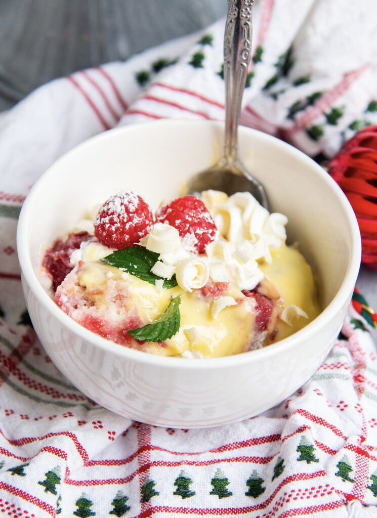A serving of trifle in a bowl topped with fresh raspberries.