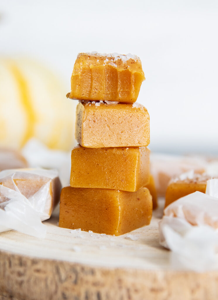 A stack of four pumpkin spice caramels topped with sea salt, the top caramel has a bite out of it.