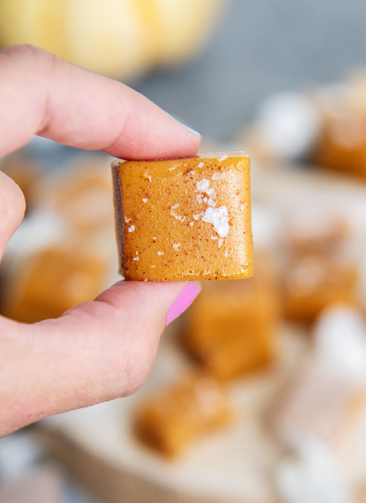 A hand holding a golden colored pumpkin spice caramel square.