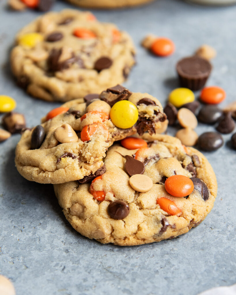 A pile of two peanut butter cookies packed with peanut butter cups and reeses pieces.