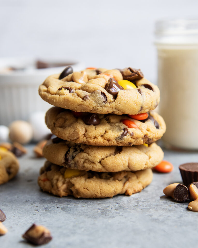 A stack of four loaded peanut butter cookies next to a glass of milk.