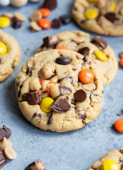 A pile of two peanut butter cookies packed with peanut butter cups and reeses pieces.
