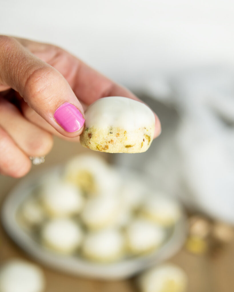 A hand holding a pistachio snowball cookie with vanilla icing on top.