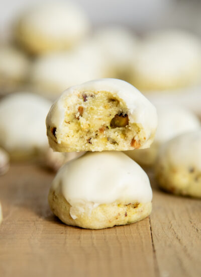 A stack of two pistachio drop cookies, and the top cookie has a bite out of it.