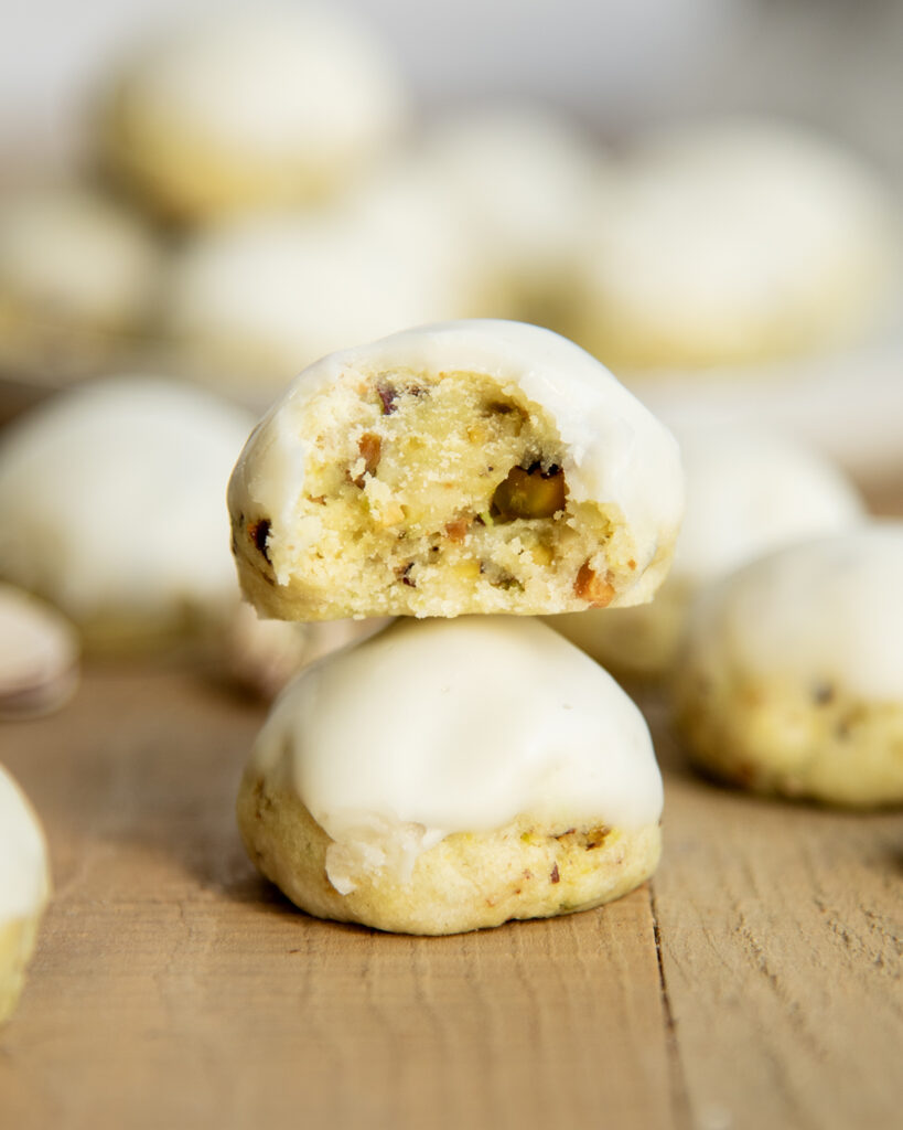 A stack of two pistachio drop cookies, and the top cookie has a bite out of it.
