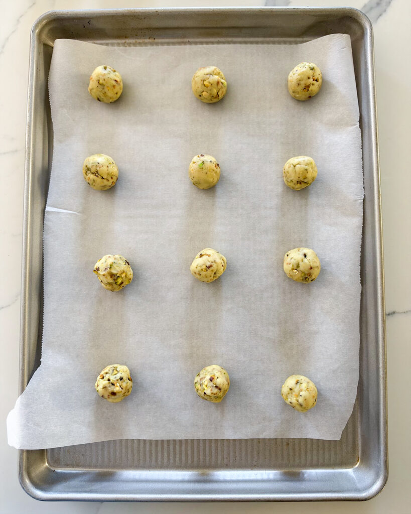 Pistachio snowball cookie dough balls on a cookie sheet.