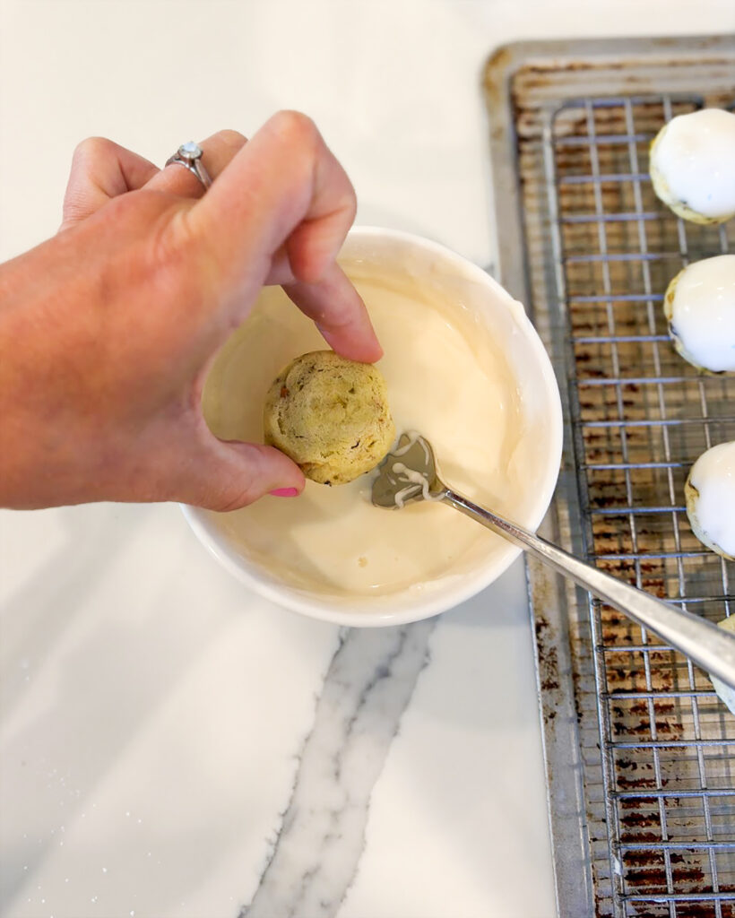 A pistachio cookie being dipped into vanilla icing in a bowl.
